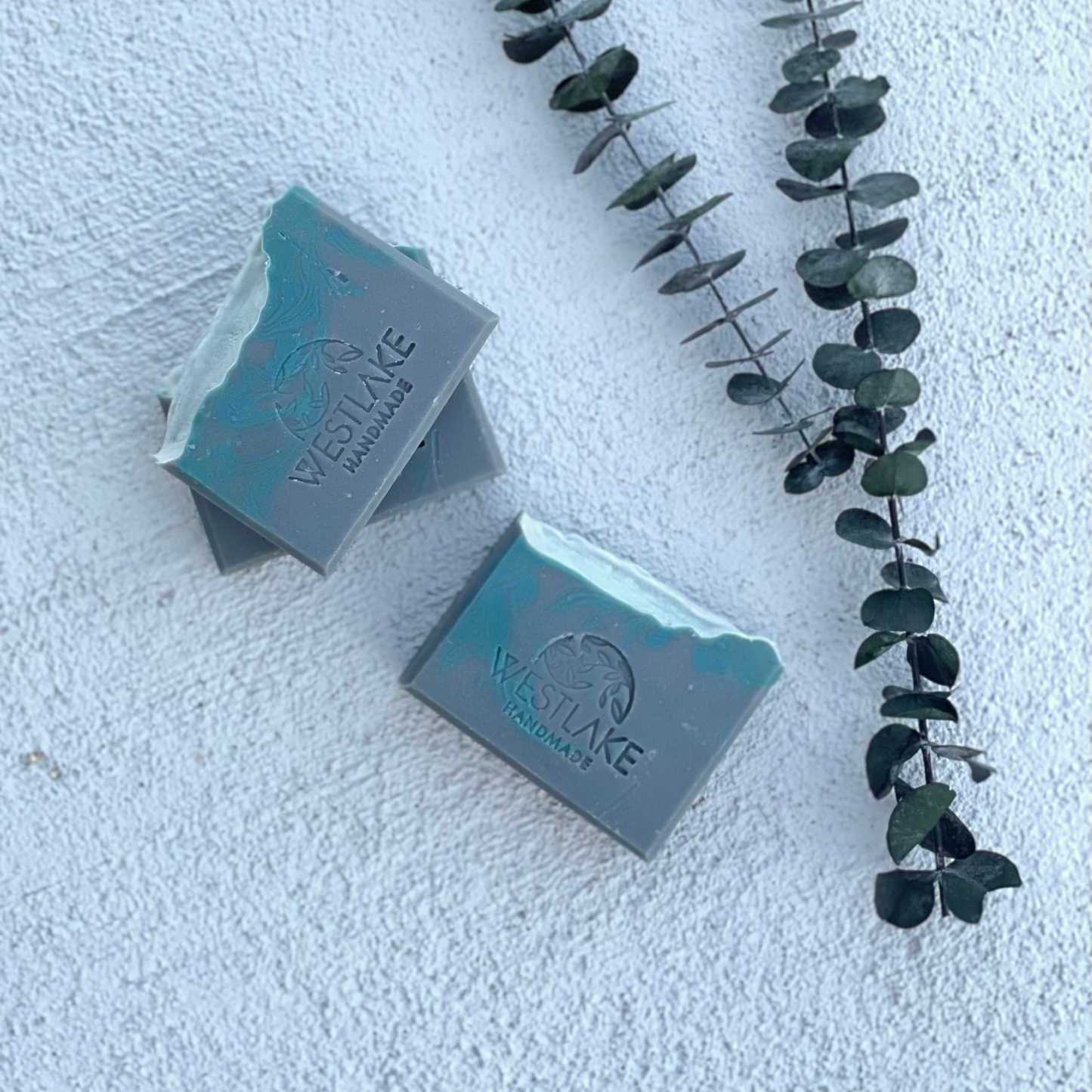 Two bars of Westlake Handmade soap on a textured white surface with eucalyptus leaves.
