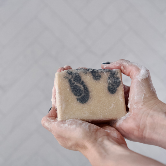Hand holding a bar of soap with blue swirls against a neutral background