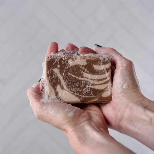Hand holding a Westlake Handmade bar of soap with a marbled design against a neutral background
