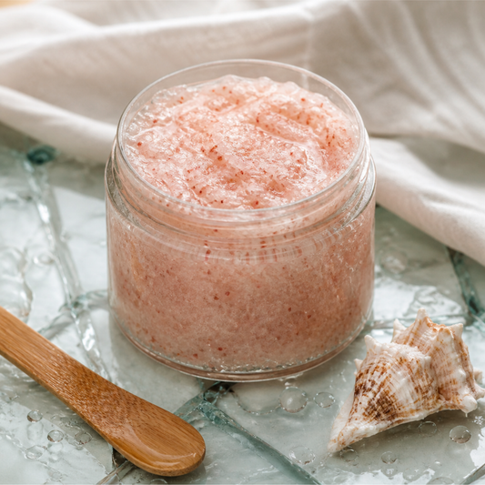 Glass jar of pink scrub with a wooden spoon on a textured surface