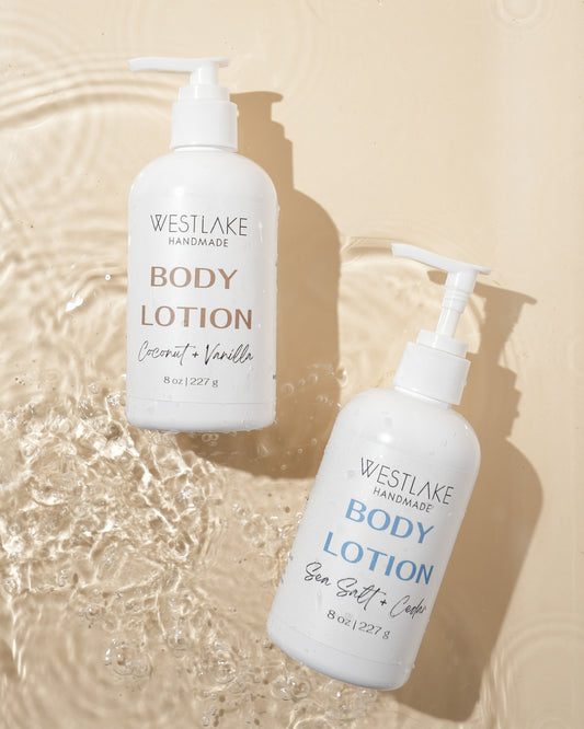Two bottles of Westlake Handmade body lotion on a beige background with water effect.