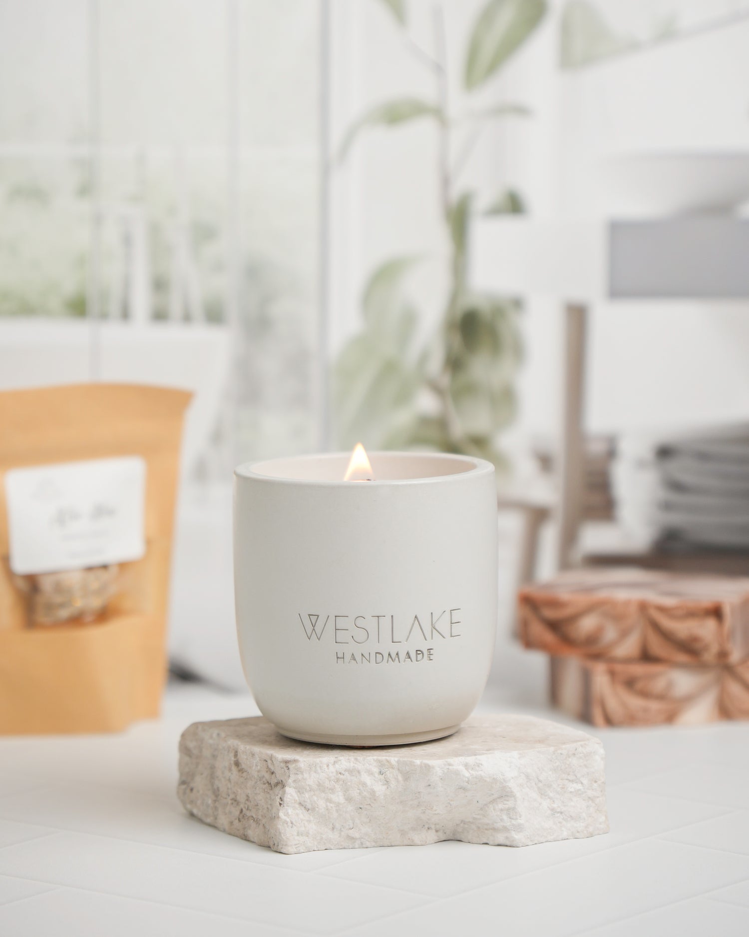 Westlake Handmade candle in a white container on a stone coaster with a blurred indoor background