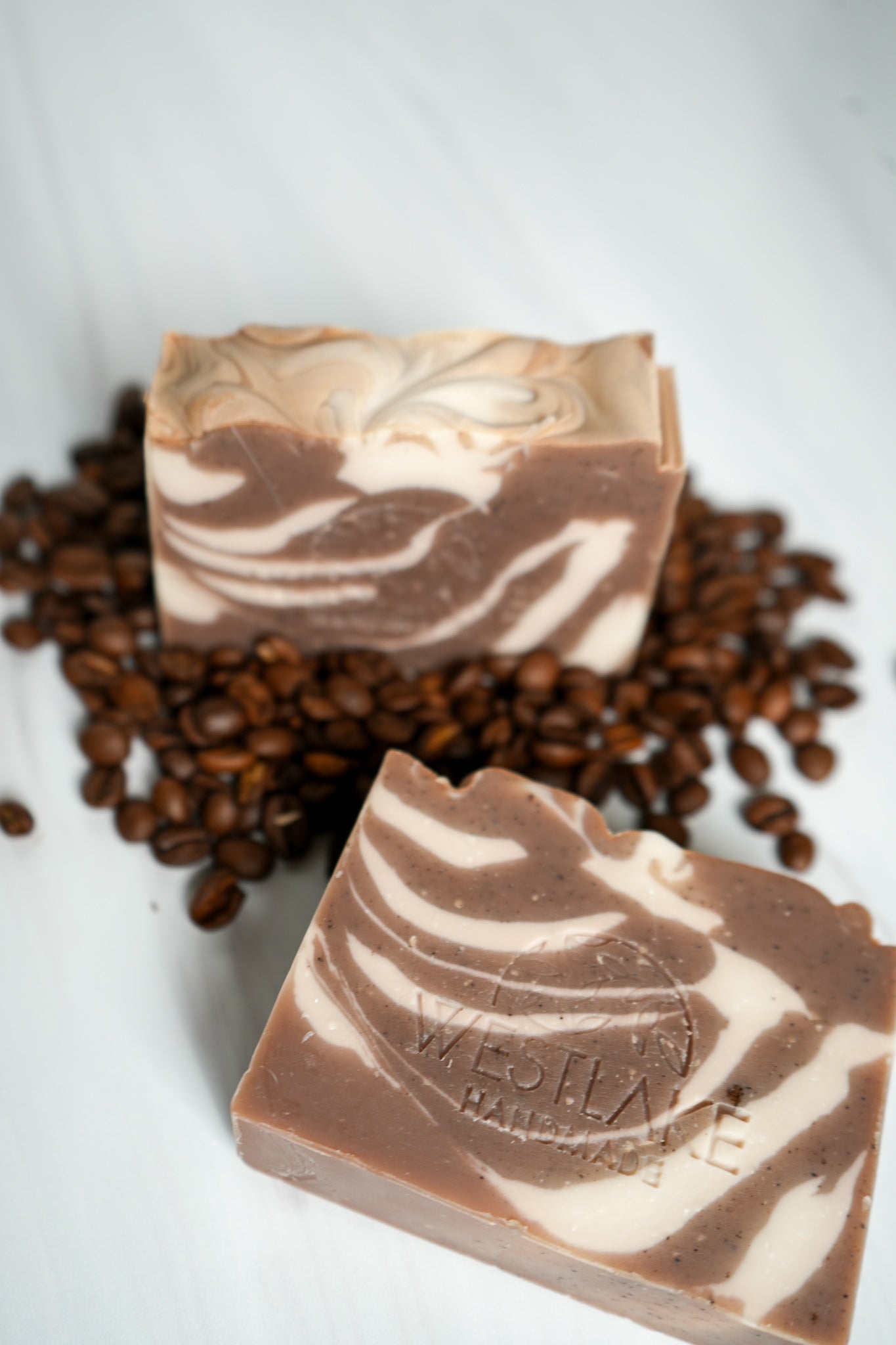 Two bars of marbled soap with coffee beans on a white background