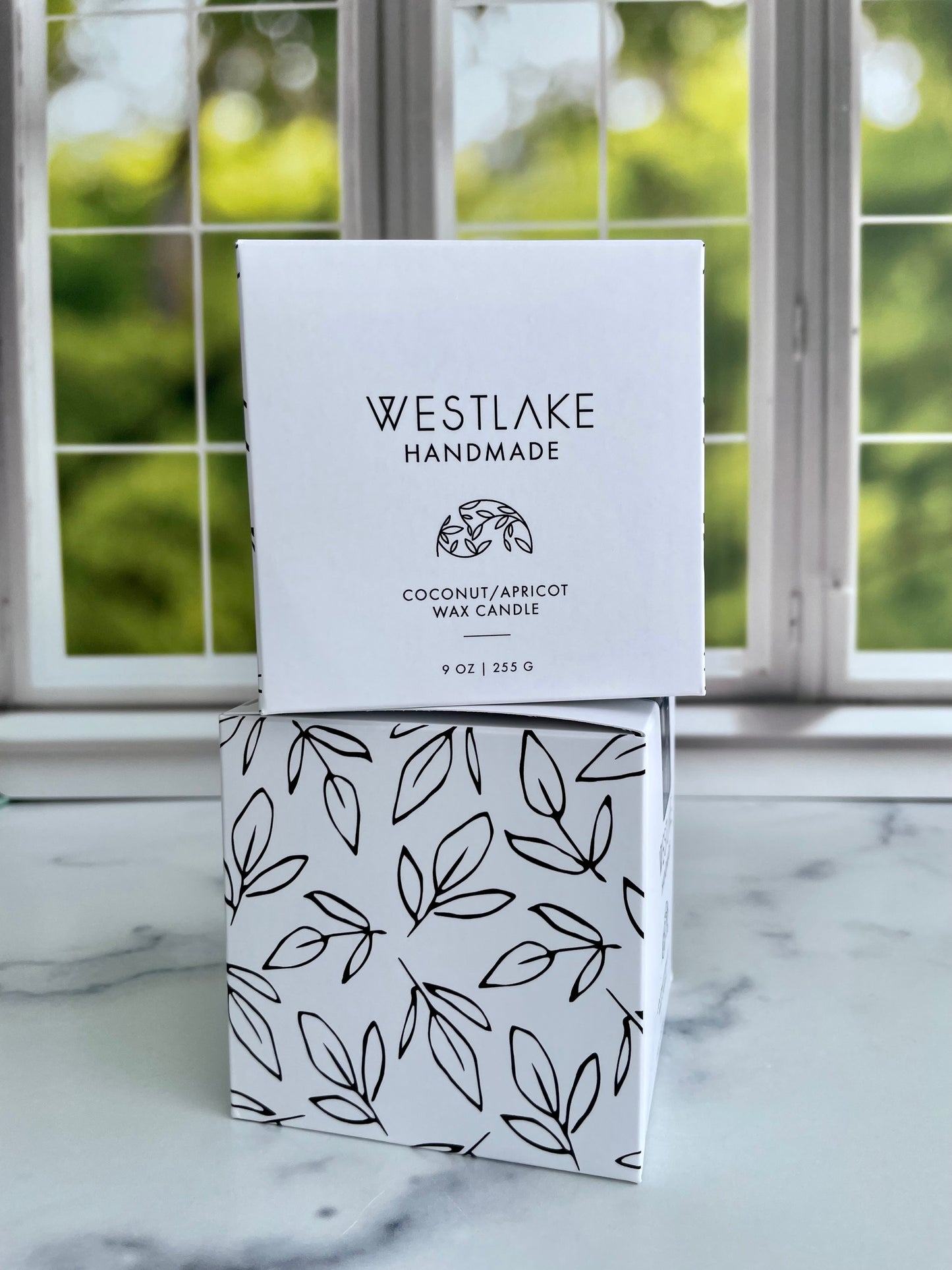 Westlake Handmade coconut apricot wax candle packaging on a marble surface with a window in the background.