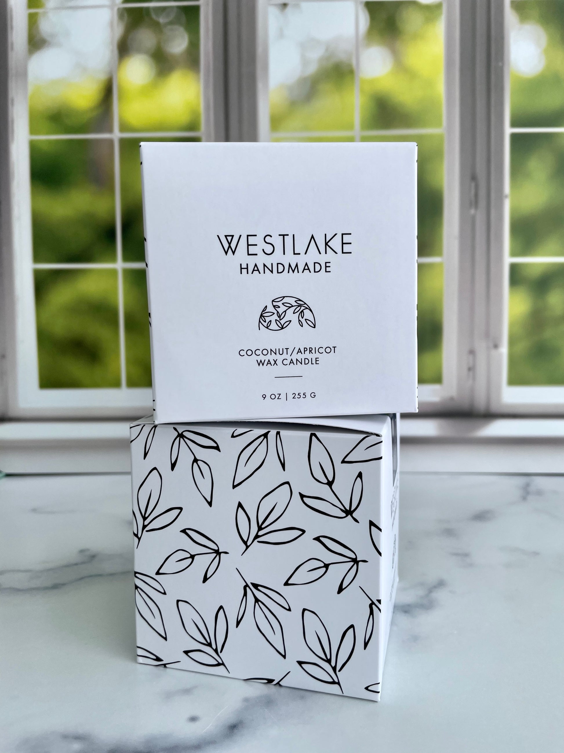 Westlake Handmade coconut apricot wax candle packaging on a marble surface with a window in the background.