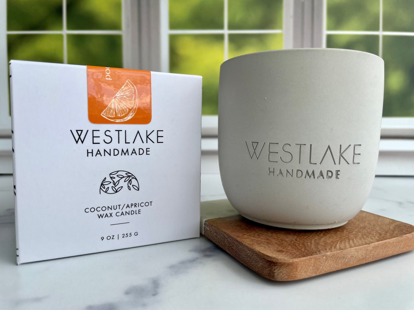 Westlake Handmade candle and packaging on a windowsill with a blurred green outdoor background