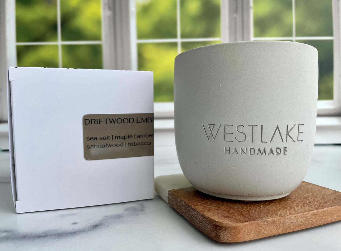Westlake Handmade concrete candle on a wooden coaster, next to a white box with 'Driftwood Ember' label.