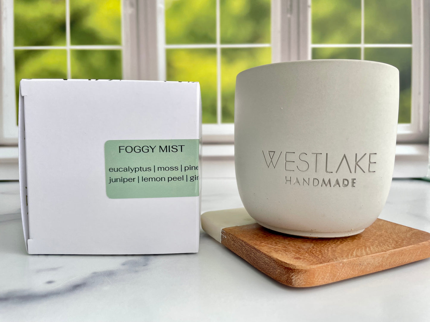 Westlake Handmade concrete candle on a wooden coaster next to a Foggy Mist candle box.