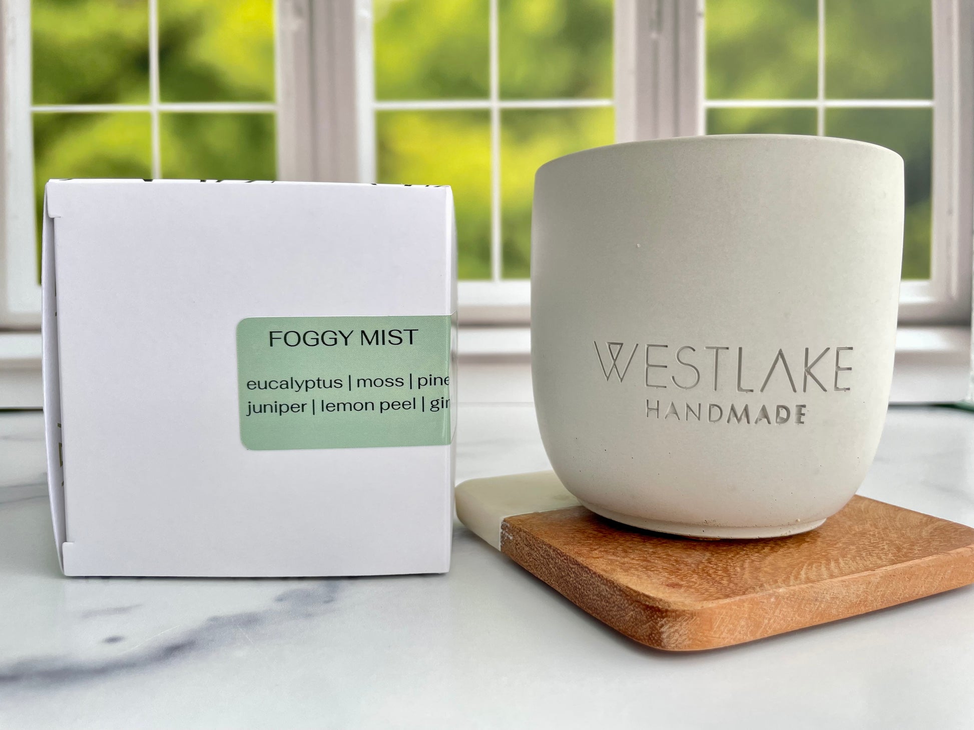 Westlake Handmade concrete candle on a wooden coaster next to a Foggy Mist candle box.