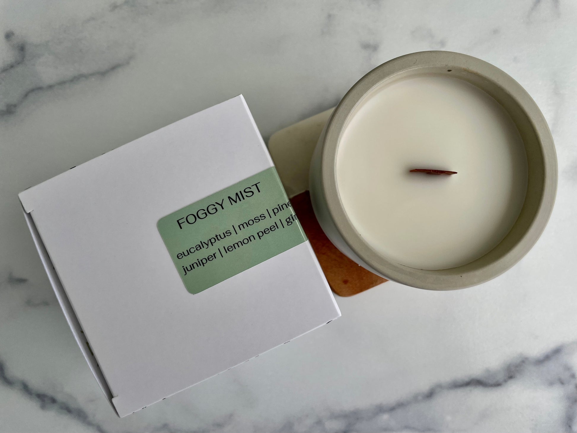 Candle labeled 'Foggy Mist' next to its packaging on a marble surface