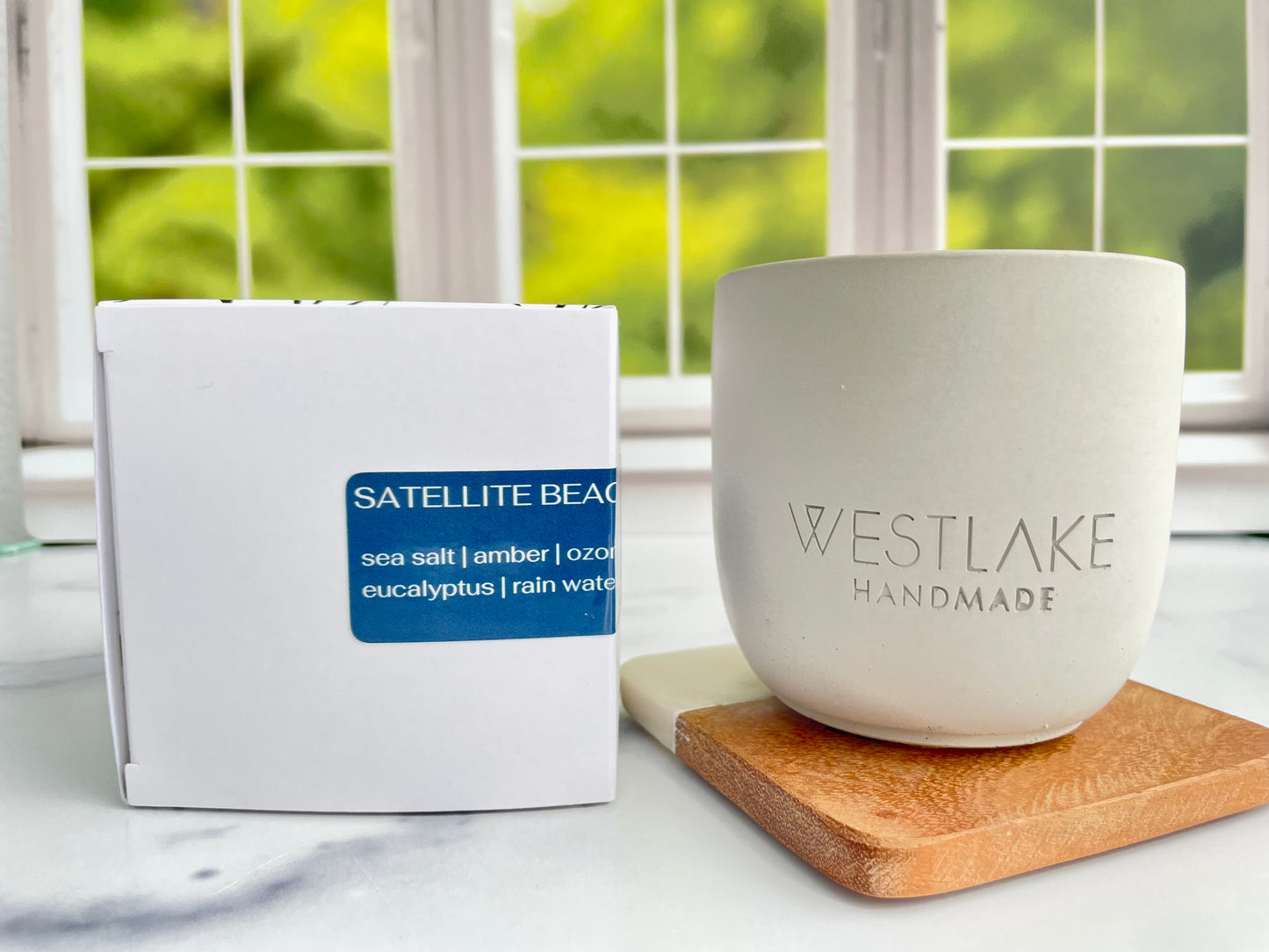 Westlake Handmade concrete candle on a wooden coaster next to a white box labeled 'Satellite Beach'.